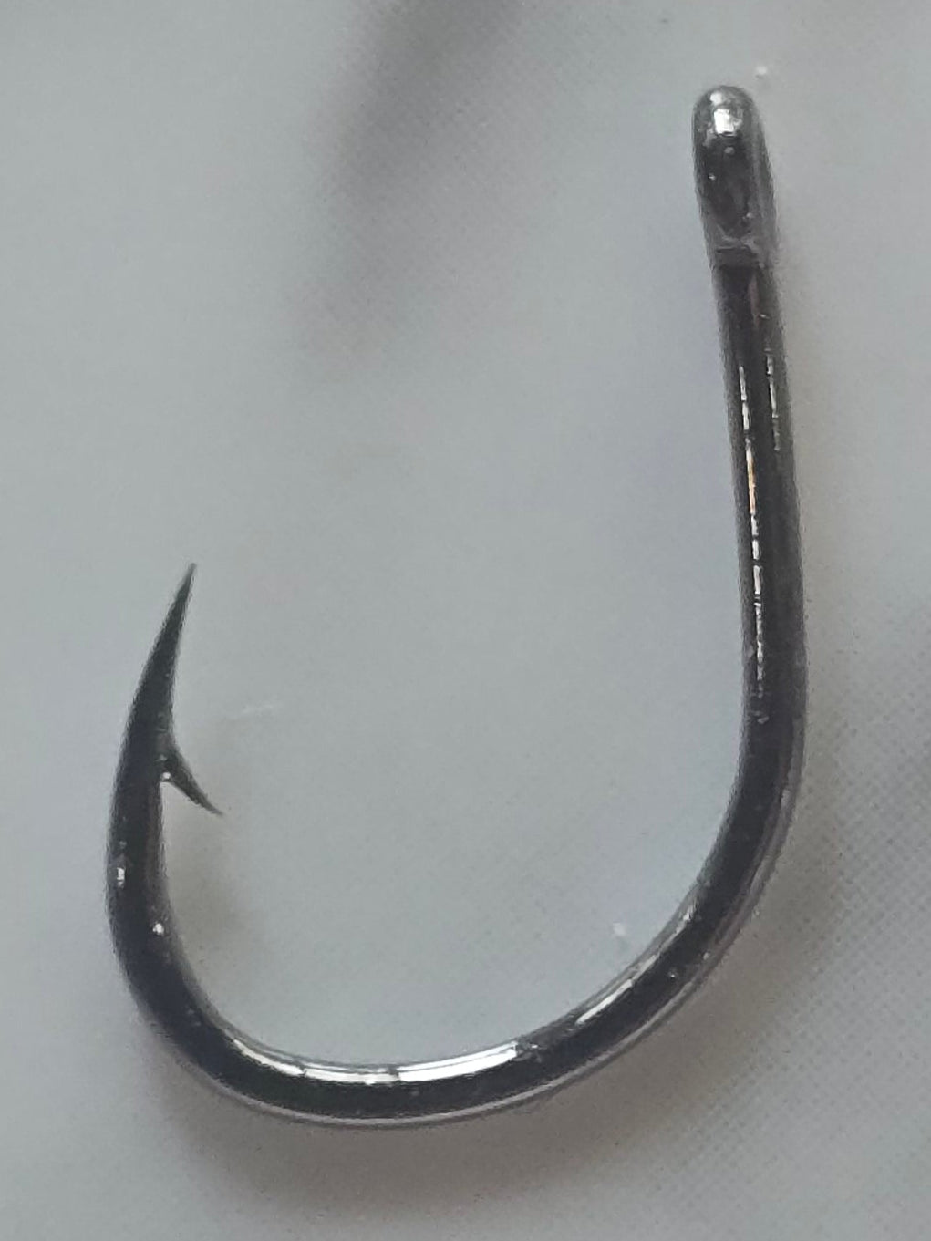 A single metallic silver fishing hook placed on a white marble surface with gray veining.