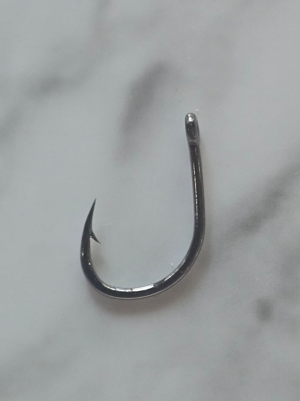 A single metallic silver fishing hook placed on a white marble surface with gray veining.