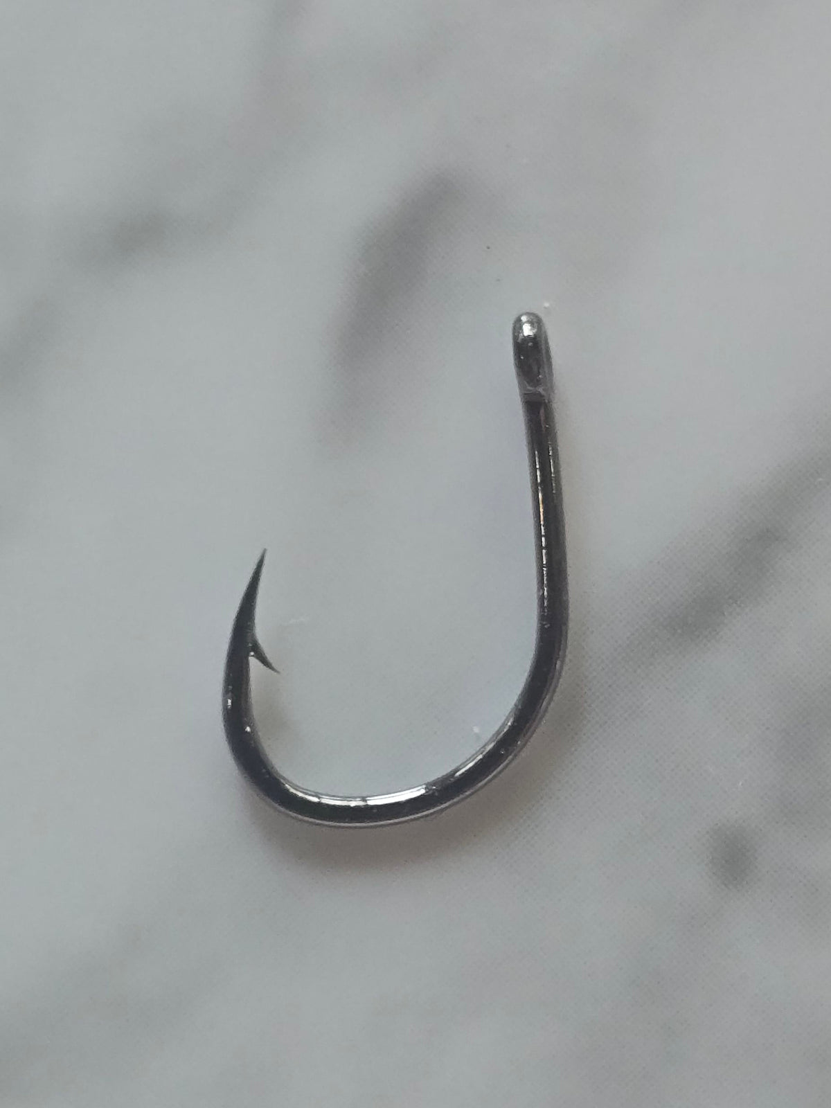 A single metallic silver fishing hook placed on a white marble surface with gray veining.